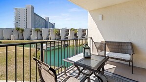 A balcony with a table and chairs, overlooking a body of water and a row of buildings. - Ocean View 2BR Condo • Pets • Balcony • Sleeps 8 (Panama City Beach)