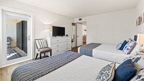 A bedroom with two beds, a TV, a dresser, and a door leading to another room. - Ocean View 2BR Condo • Pets • Balcony • Sleeps 8 (Panama City Beach)