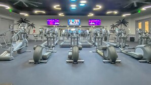 A gym with multiple treadmills and elliptical machines, a TV screen, and a wall with palm trees. - Snowbird-friendly condo with pool, hot tub, splash area, tennis, restaurant, gym (Destin)