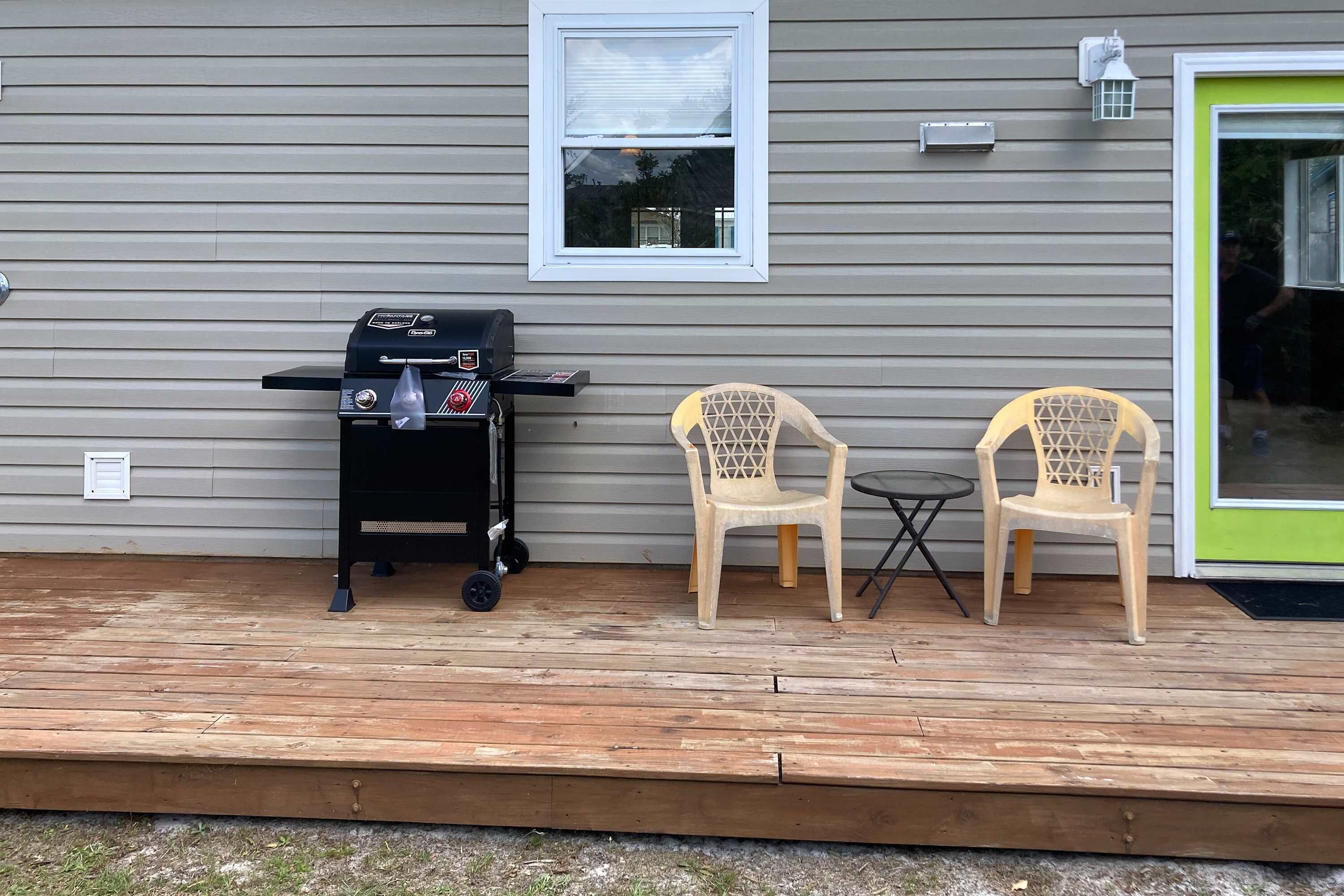 A wooden deck with a grill and two chairs.