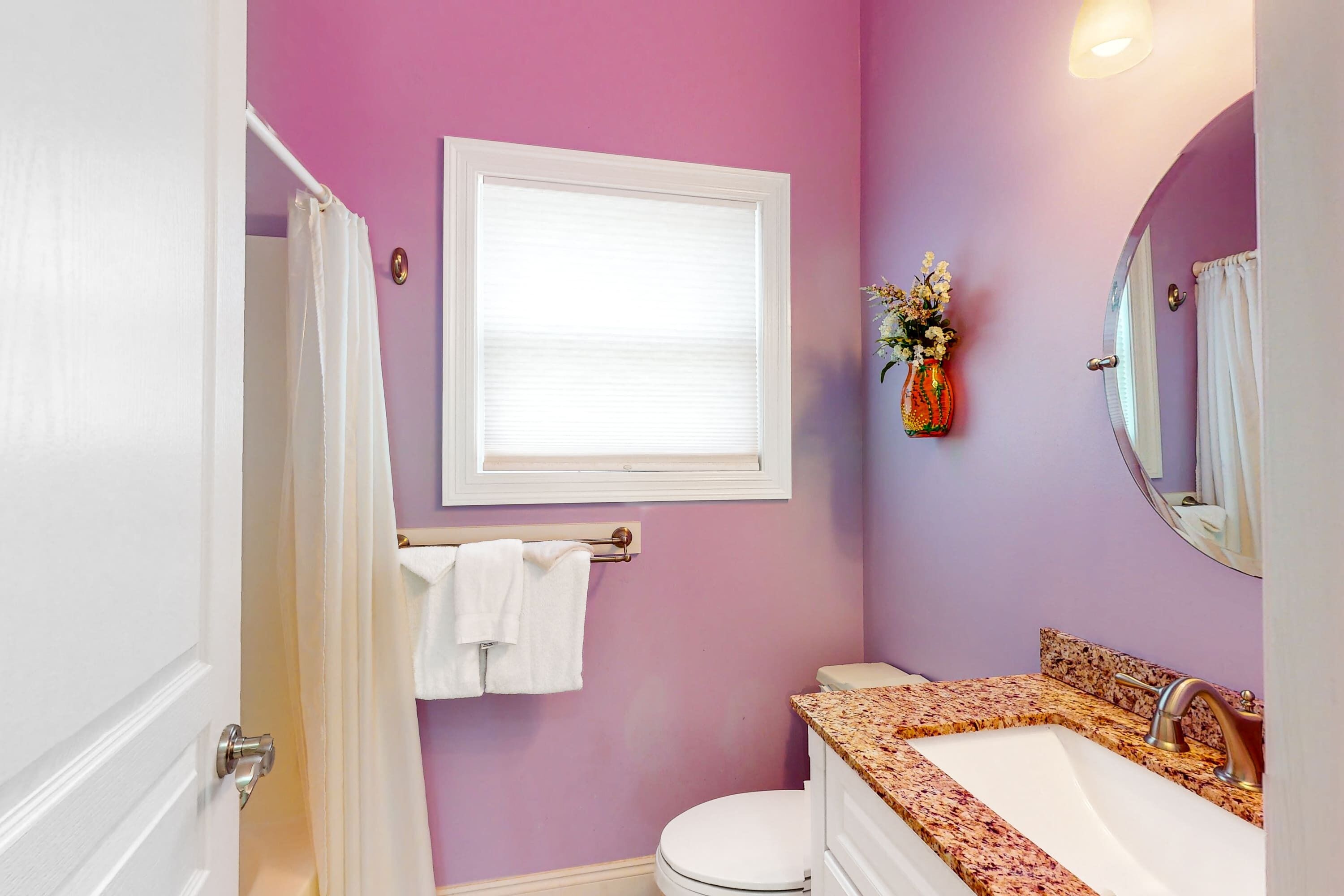 Une salle de bain équipée de toilettes, d’un lavabo et d’une fenêtre avec des stores.