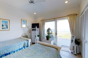 A bedroom with two beds, a TV, a dresser, and a balcony with curtains. - King's Crown (St. George Island)
