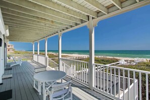 Eine überdachte Terrasse mit Tisch und Stühlen mit Blick auf Strand und Meer.