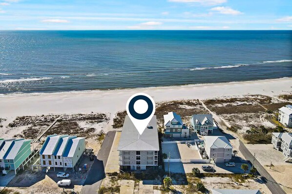 An aerial view of a coastal area with a large building complex, including a hotel with multiple rooms and a parking area.