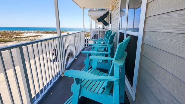 A balcony with turquoise Adirondack chairs, a view of the beach, and a white railing.