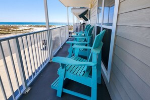 Varanda com cadeiras Adirondack cor turquesa, vista para a praia e guarda-corrimão branco.