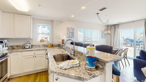 A modern kitchen with white cabinets, granite countertops, a sink, and a dining area with a blue chair and a chandelier.