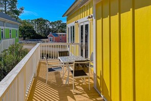 A yellow building with a balcony featuring a table and chairs, a white railing, and a view of neighboring houses. - Beautiful, dog-friendly cottage with deck & patio - stroll to Carrabelle Beach (Carrabelle)