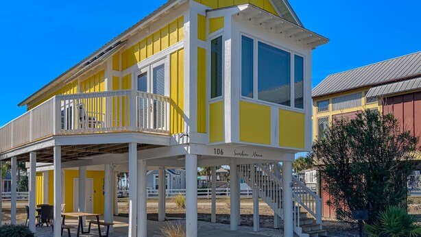 A yellow and white beach house with a balcony, numbered 106, and a covered outdoor seating area. - Beautiful, dog-friendly cottage with deck & patio - stroll to Carrabelle Beach (Carrabelle)
