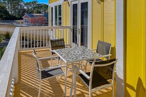 A balcony with a table and chairs, a white railing, and a yellow building in the background. - Beautiful, dog-friendly cottage with deck & patio - stroll to Carrabelle Beach (Carrabelle)