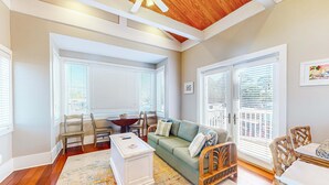 A cozy living room with a wooden ceiling, a green sofa, wicker chairs, a white coffee table, and large windows with blinds. - Beautiful, dog-friendly cottage with deck & patio - stroll to Carrabelle Beach (Carrabelle)