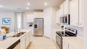 Une cuisine moderne avec des meubles blancs, des appareils en acier inoxydable et un plancher en bois.