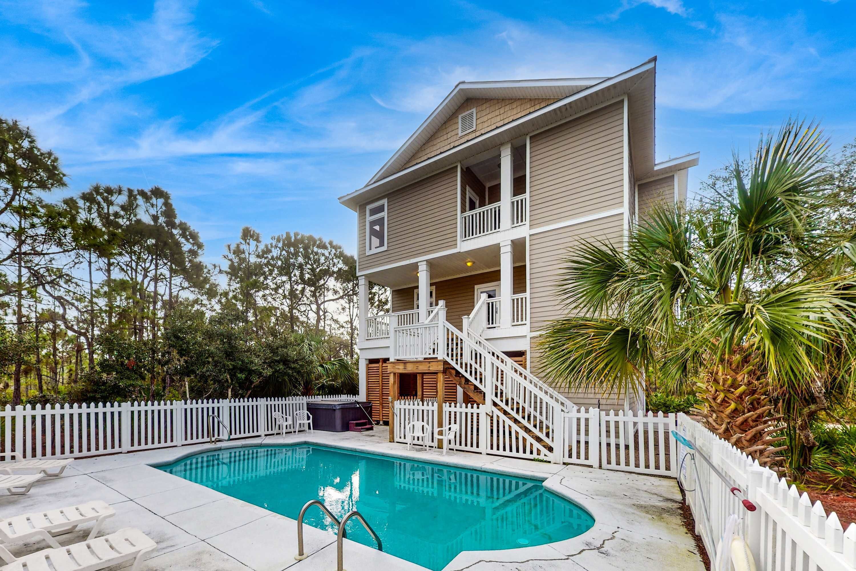 A two-story house with a swimming pool, white picket fence, and a wooden deck.