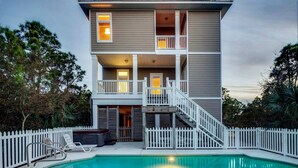 A two-story house with a balcony on the second floor, a pool in the front yard, and a white picket fence. - Spacious dog-friendly home with pool, hot tub, access to tennis, pickle ball, pools (St. George Island)