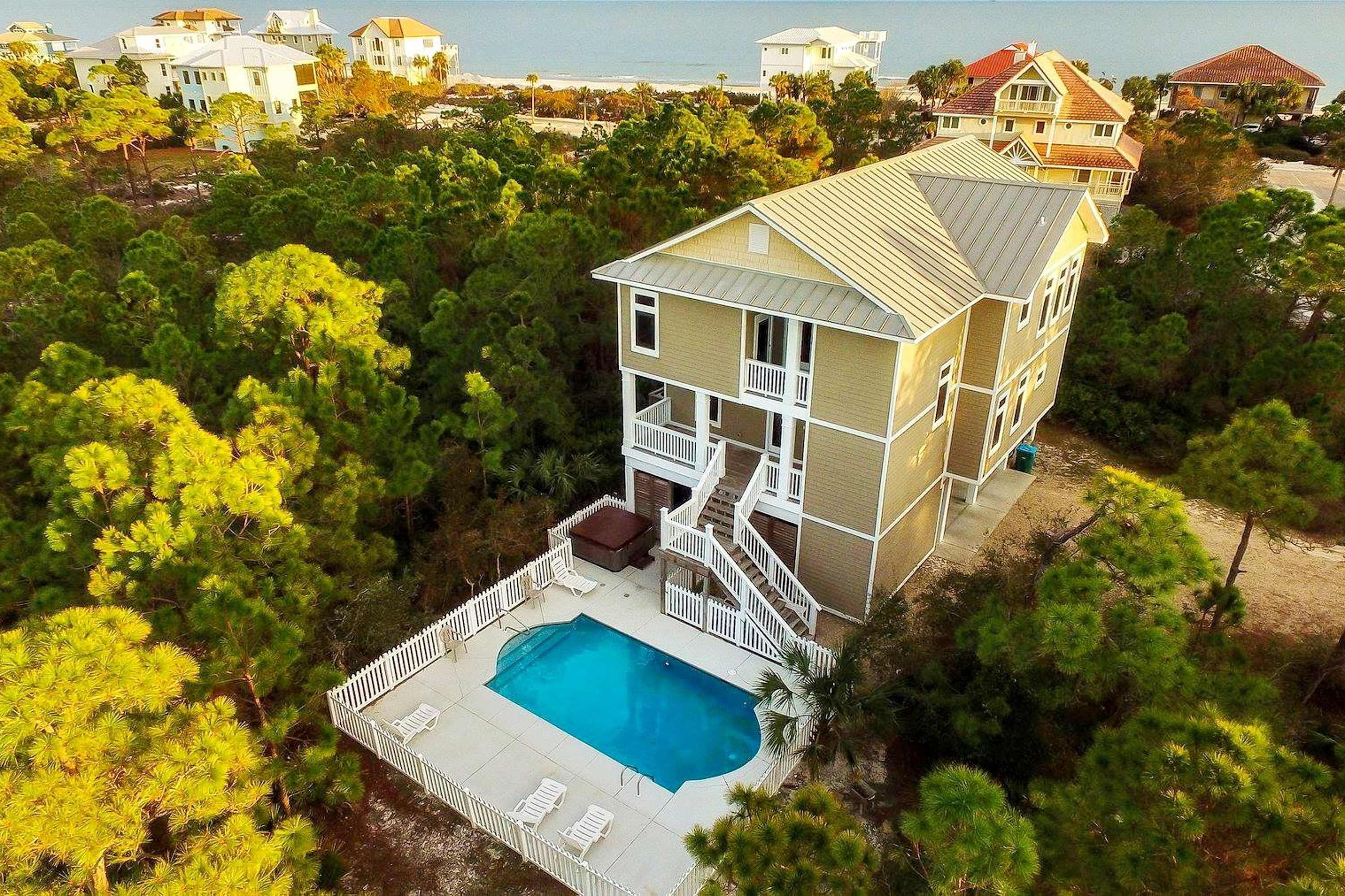 Una casa de dos pisos con piscina, rodeada por una cerca blanca.