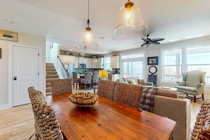 Ein geräumiges Wohnzimmer mit einem Holzesstisch, gemusterten Sofas und einer Küche im Hintergrund.