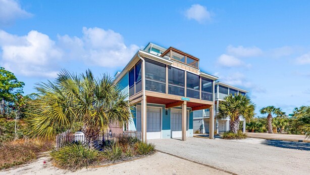 Een tweelaags strandhuis met een balkon, grote ramen en een overdekte veranda.
