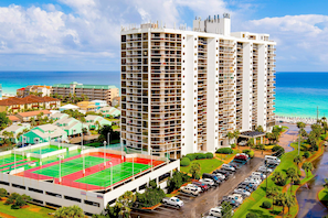 A high-rise hotel with multiple floors, a tennis court, and a parking area.