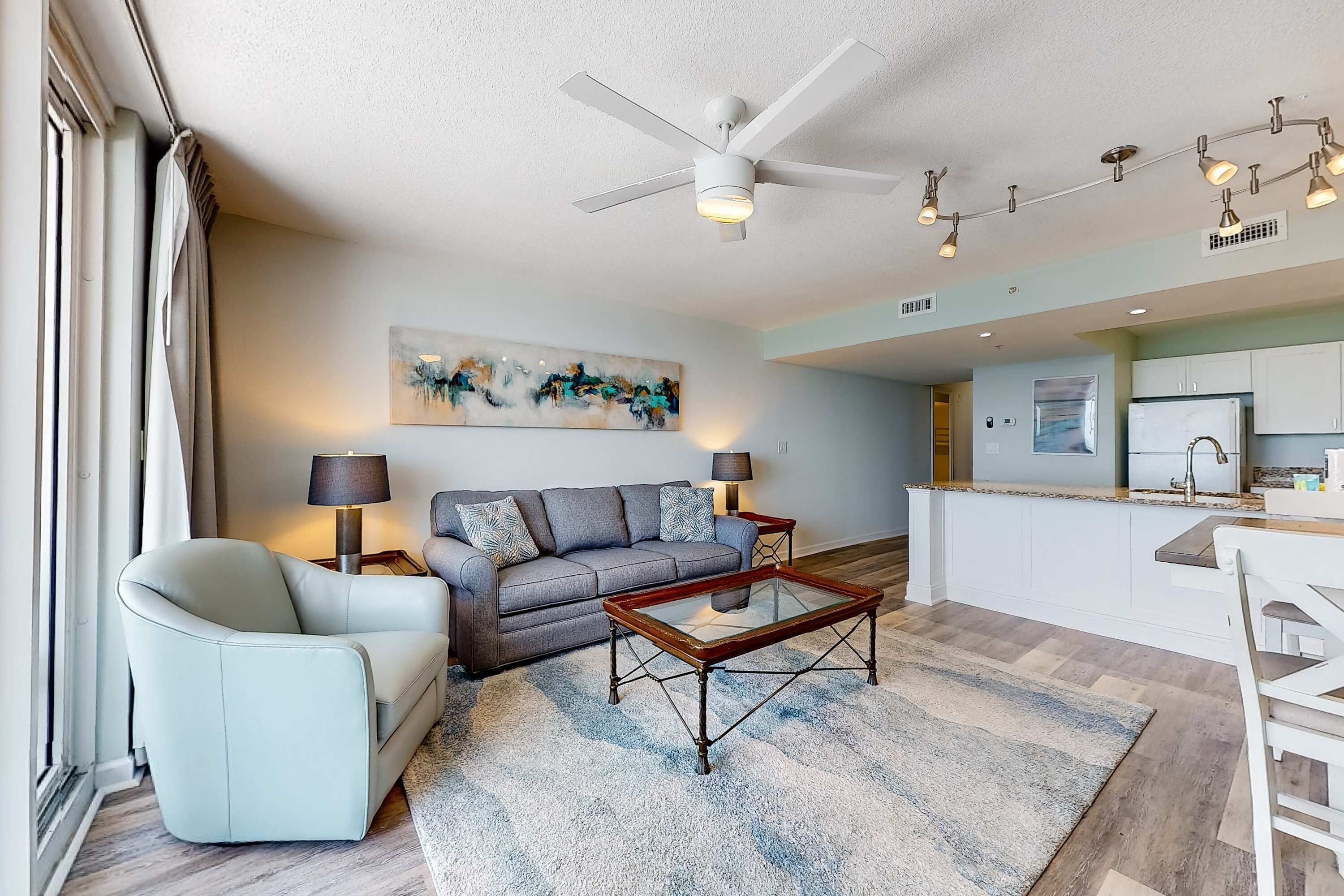 A modern living room with a sofa, armchair, coffee table, and a ceiling fan.