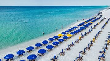Une plage bordée de rangées de parasols bleus et jaunes et de chaises longues.