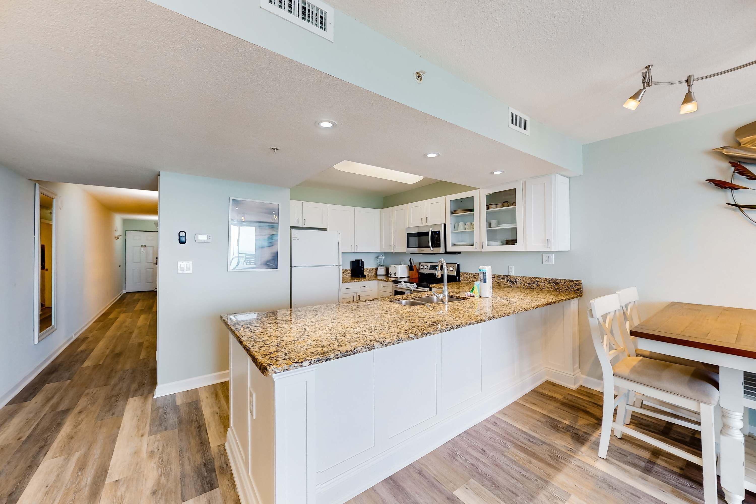 A modern kitchen with white cabinets, granite countertops, and a dining area with a wooden table and white chairs.