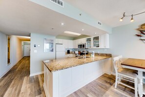 Eine moderne Küche mit weißen Schränken, Granit-Arbeitsplatten und einem Essbereich mit einem Holztisch und weißen Stühlen.