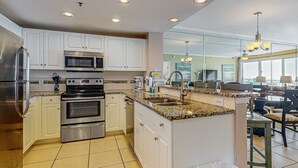 A modern kitchen with white cabinets, stainless steel appliances, and a granite countertop. - Inviting & sleek condo w private balcony, shared pool, grill & fitness center (Destin)