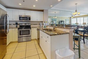 A modern kitchen with white cabinets, stainless steel appliances, and a granite countertop. - Inviting & sleek condo w private balcony, shared pool, grill & fitness center (Destin)
