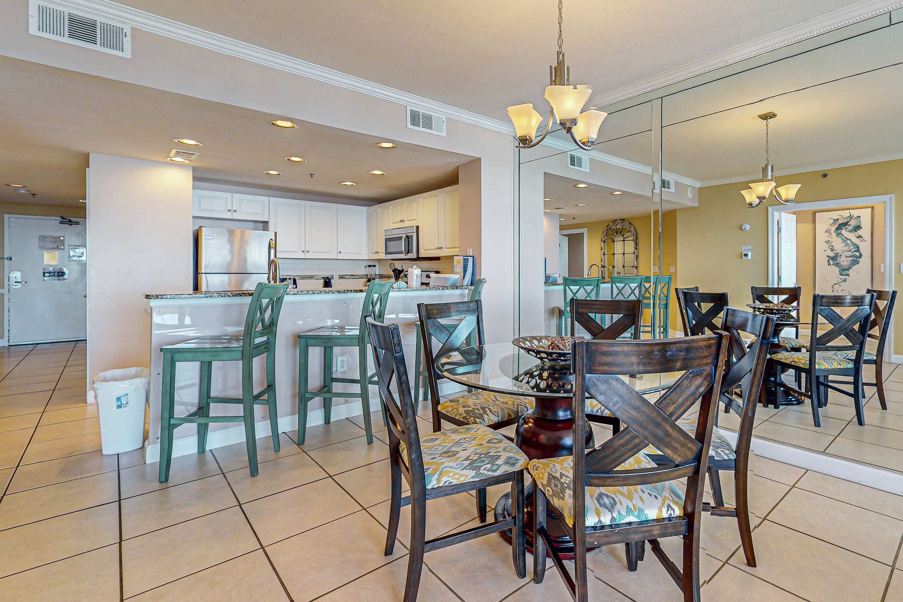 A spacious dining area with a central island, surrounded by chairs and a chandelier.