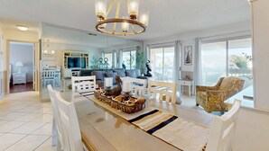 Amplia sala de estar con un gran candelabro, mobiliario blanco y vistas al exterior a través de amplias ventanas.