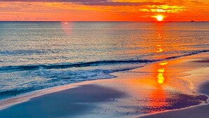 Una playa con el sol poniéndose sobre el océano, creando un reflejo en la arena mojada.