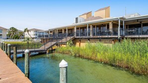 Un hotel frente al agua con una terraza de madera, un paseo techado y un puente que conecta con otro edificio.