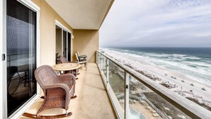 Een balkon met rieten meubels, een glazen deur en uitzicht op het strand.