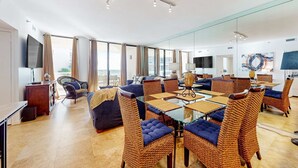 A modern living room with a glass dining table, wicker chairs, a sofa, and a TV. - East Pass Towers 302 (Destin)