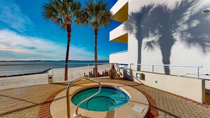 A swimming pool with a metal ladder, surrounded by a brick walkway, palm trees, and a view of the sea. - East Pass Towers 302 (Destin)