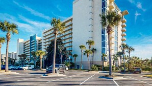 Un hotel moderno con diversi piani, palme e un parcheggio.
