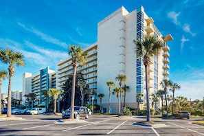 A modern hotel with multiple floors, palm trees, and a parking lot. - Airy Beachfront Condo w Shared Outdoor Pool, Central AC, Free WiFi (Destin)