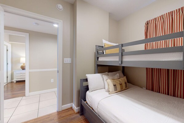 Un dormitorio con una cama litera, una mesita de noche y una cortina a rayas.
