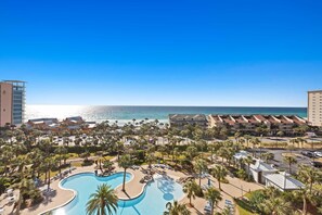Un resort con una piscina grande, villas frente a la playa y una vista despejada del océano.