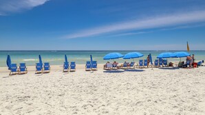 Una spiaggia con file di sedie e ombrelloni blu, cielo sereno e l'oceano sullo sfondo.
