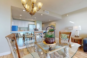 A dining area with a glass table, chairs, and a chandelier. - Airy Beachfront Condo w Shared Outdoor Pool, Central AC, Free WiFi (Destin)
