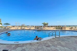Una piscina con sillas de descanso y sombrillas, una torre de salvavidas y un cielo azul despejado.