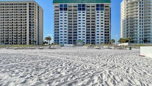 Et strandhotel med flere etager, en sandstrand i forgrunden og en klar blå himmel.
