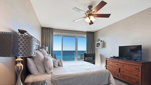 Ein Schlafzimmer mit Bett, Kommode, Fernseher, Deckenventilator und Meerblick.