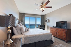 A bedroom with a bed, a dresser, a TV, a ceiling fan, and a view of the ocean. - Beach condo with private balcony, gulf views & fitness room (Destin)