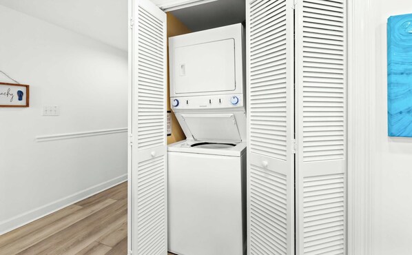 A laundry room with a front-loading washer and dryer, white walls, and a wooden floor. - Marvelous Gulf-front condo with amazing views, pool, snack bar, & fitness room (Destin)