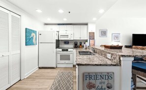 Eine moderne Küche mit weißen Schränken, einem Kühlschrank, einem Backofen und einer Mikrowelle. An den Wänden befinden sich gerahmte Bilder und ein Schild mit der Aufschrift 'FRIENDS are like.'