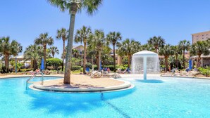 Ein Swimmingpool mit einer Fontäne, umgeben von Palmen und Liegestühlen, typisch für ein Resort.