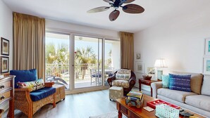 Ein großzügiges Wohnzimmer mit einem großen Schiebeglasfenster, das auf einen Balkon führt, Korbmöbeln und einem Deckenventilator.