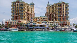 A waterfront hotel with multiple high-rise buildings, a marina with boats, and a prominent lighthouse structure. - Gulf-view condo with beach access, pool, hot tub, sauna, & private balcony (Destin)